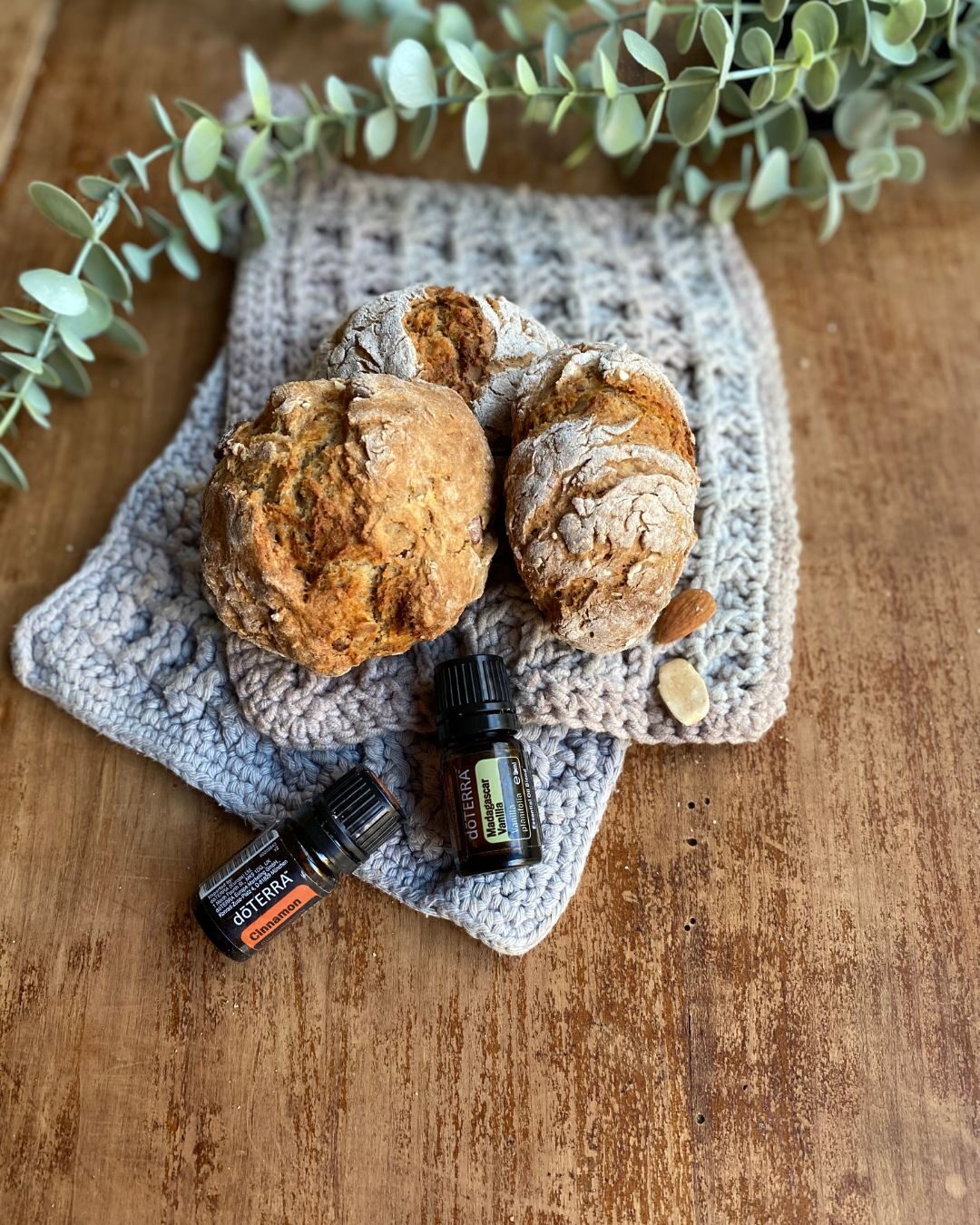 Frisch gebackene Brötchen neben Zimt- und Vanille-Öl auf einem Holztisch mit Eukalyptuszweig
